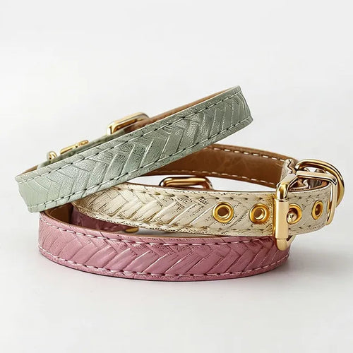 A collection of three stylish dog collars with a braided chevron texture in sage green, ivory, and dusty rose, featuring polished gold hardware and eyelets on a minimalist white surface.
