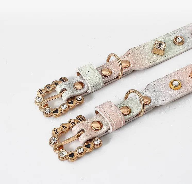 Two luxury iridescent glitter pet collars in pastel gradient colors featuring ornate gold-tone buckles with rhinestones and black heart details against a clean white background.