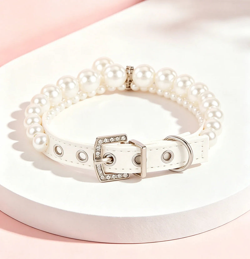 A luxury white dog collar adorned with elegant rows of large and small faux pearls, featuring a silver buckle embellished with sparkling rhinestones, displayed on a clean white circular stand.