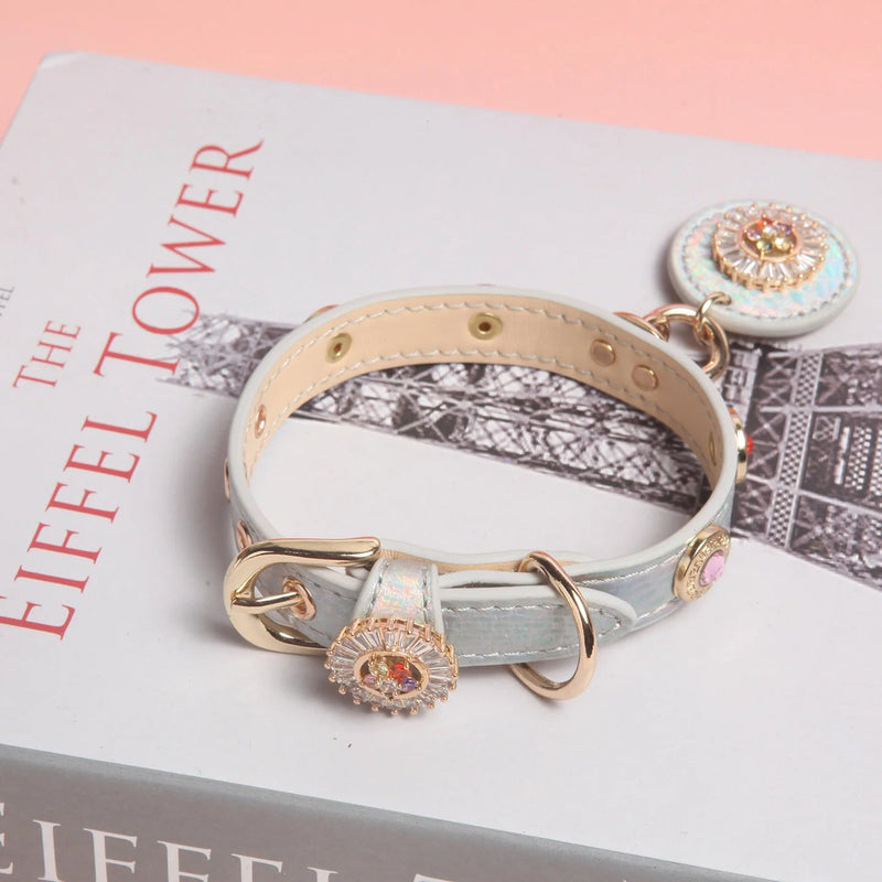 Pale iridescent leather pet collar with rhinestone medallion and gold hardware on pink background
