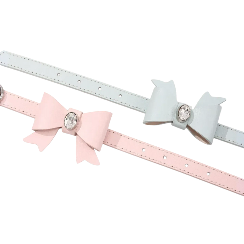 A pair of thin leather belts in pastel pink and light blue, each adorned with a large matching leather bow featuring a sparkling clear crystal center.