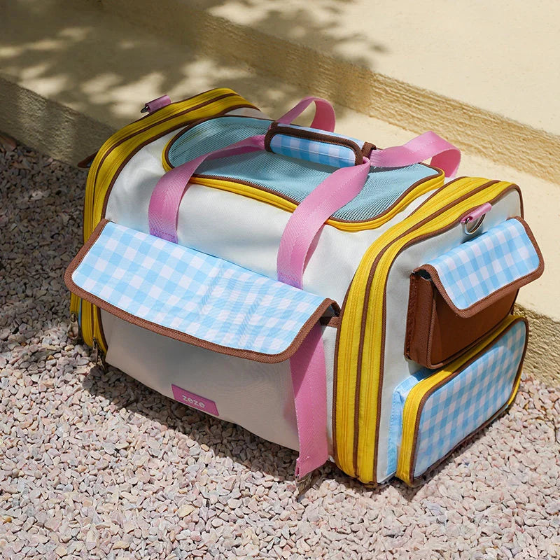 Pet travel bag showing multiple pockets, blue plaid front pocket, brown leather side pocket and pink handles