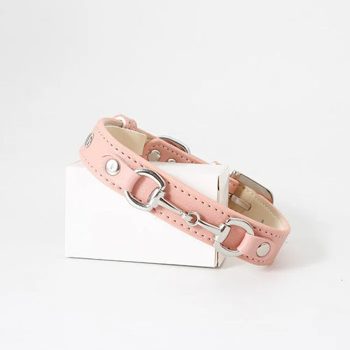 A light pink leather pet collar featuring decorative silver horse-bit hardware and round metal studs, presented on a small white box against a plain background.