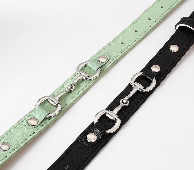Close-up of two narrow faux leather belts in mint green and black featuring silver horsebit buckle details and round metal studs on a white background.
