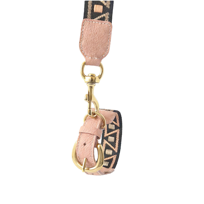 Artisan woven dog leash featuring a geometric patterned strap in tan and black, premium blush pink pebbled leather trim, and polished gold-tone hardware, shown against a solid black background.